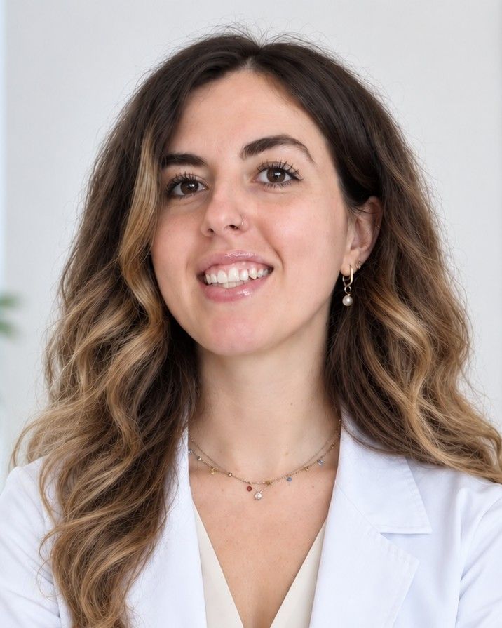 Ilaria Rizzi, nutrizionista, sorride in camice bianco nel suo studio, davanti a una parete chiara.
